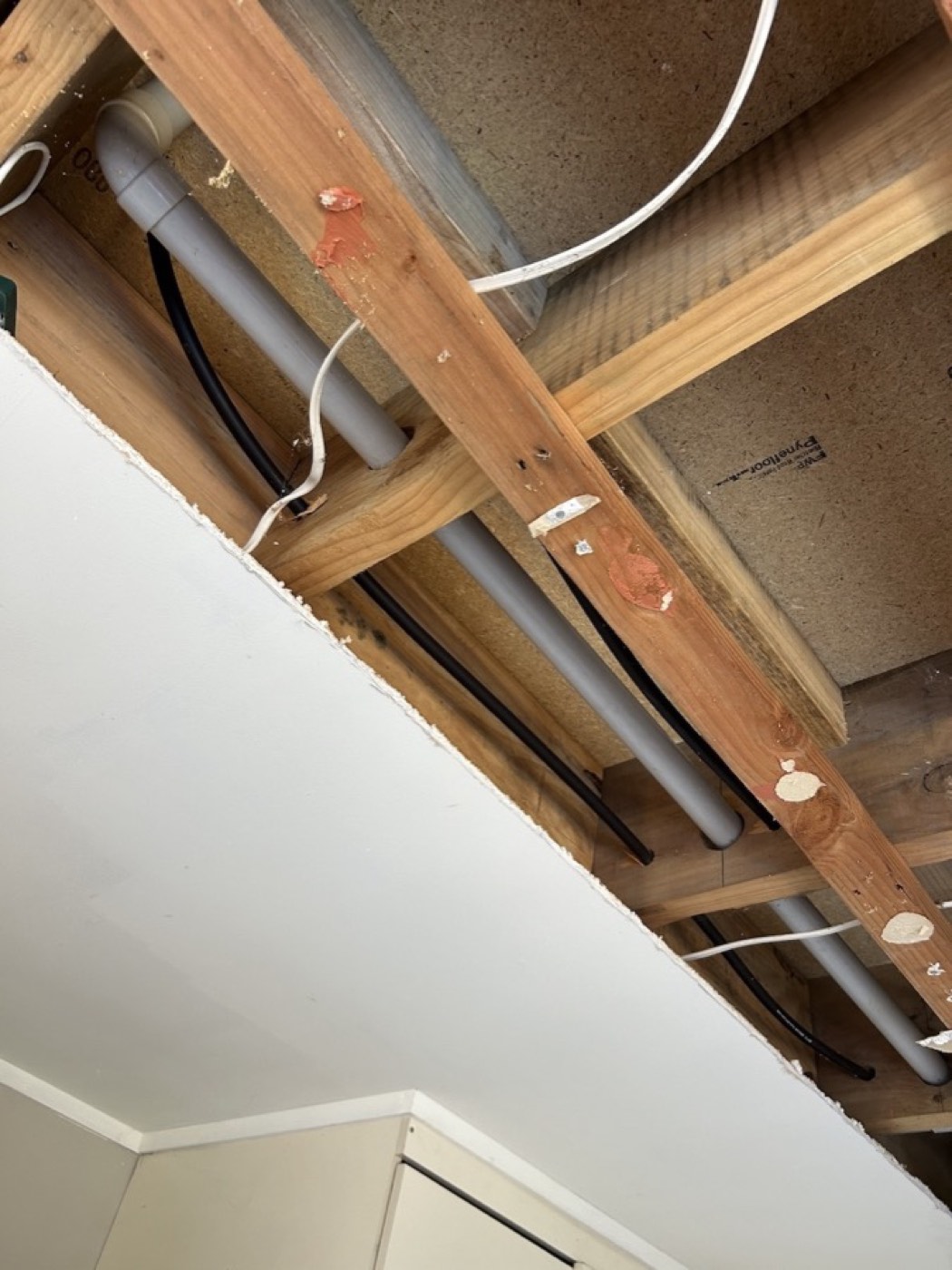 A ceiling opened along its length with new water pipe running through the joists